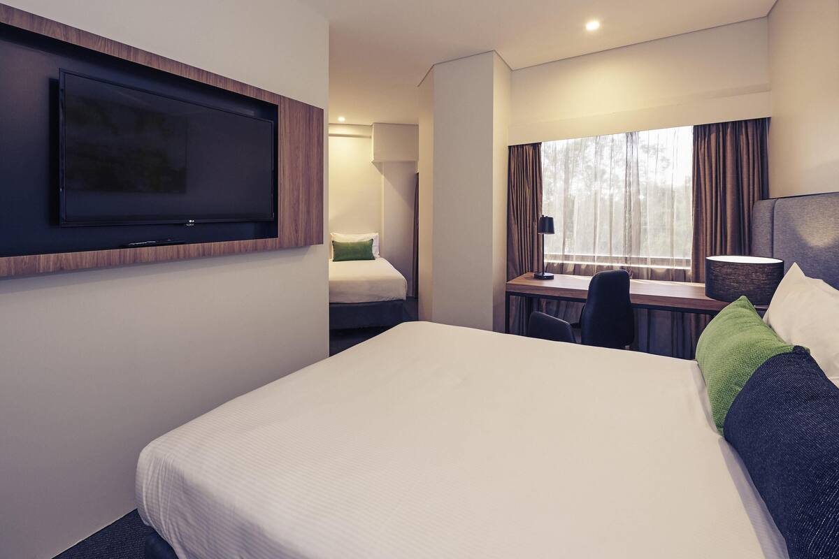 A hotel room with a bed, a desk, a chair, a TV, and a window with curtains.