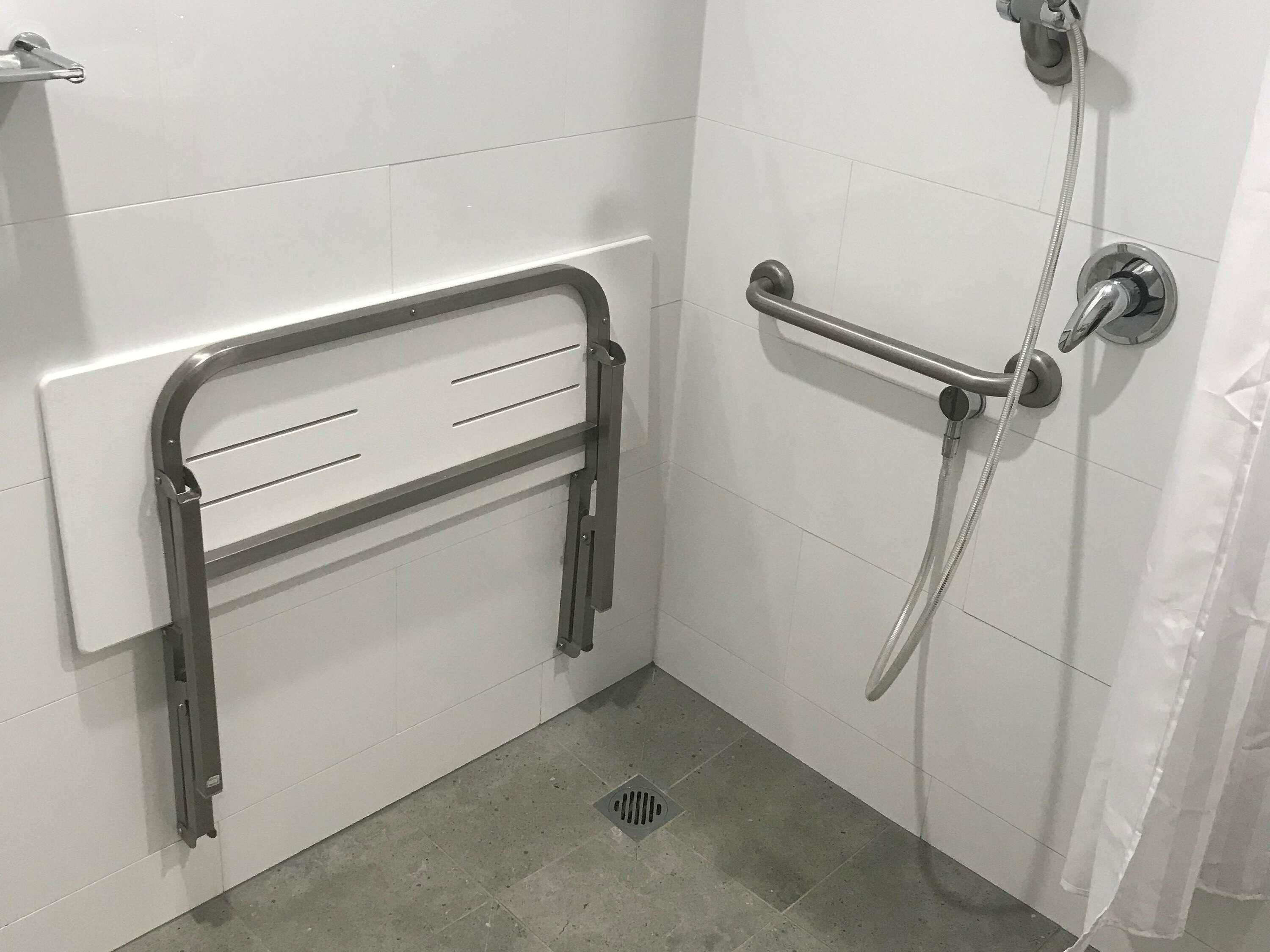 Ein Badezimmer mit weiß gefliesten Wänden, einer Dusche inklusive Handbrause und einer Haltestange.