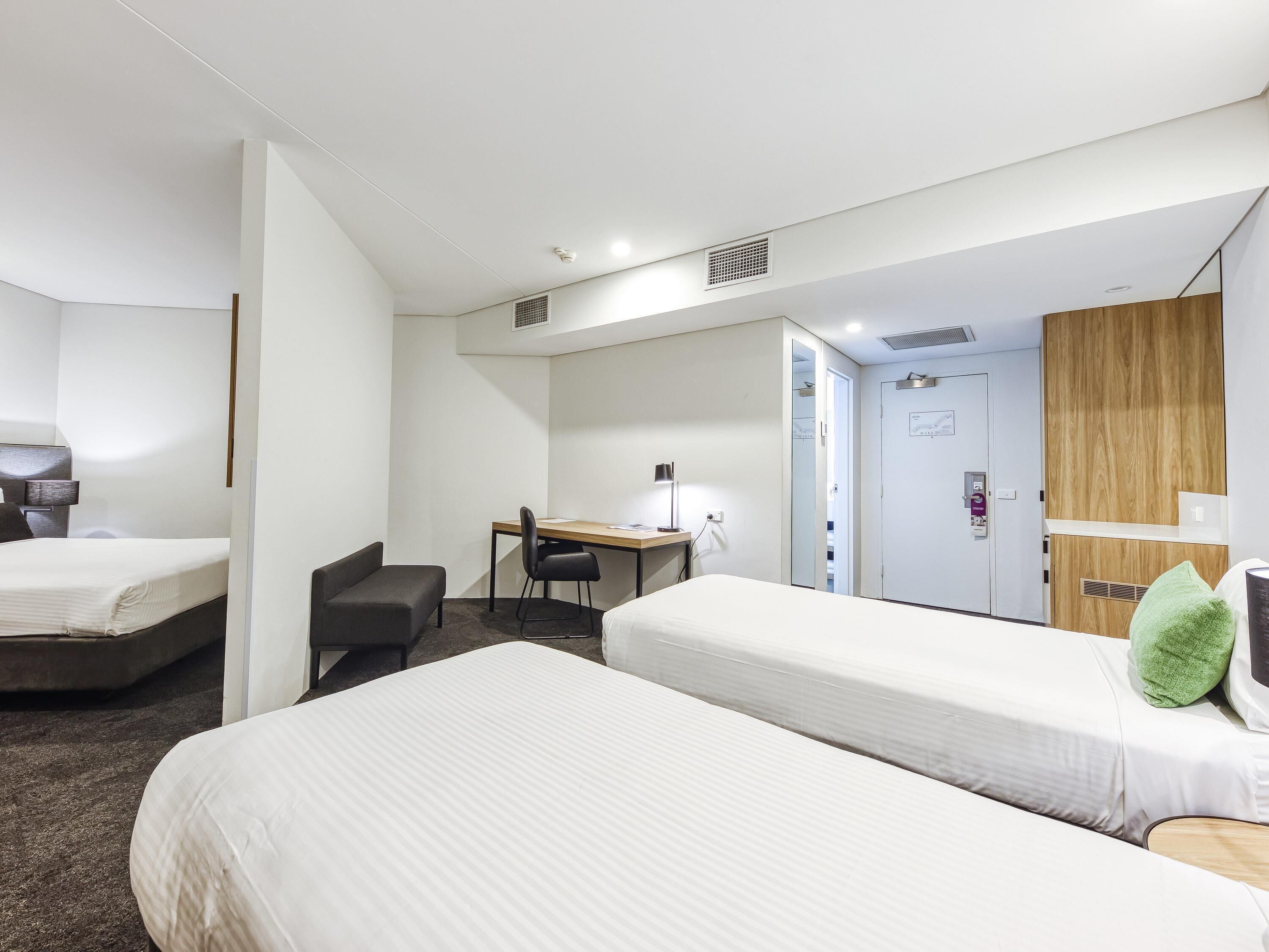 Ein Hotelzimmer mit zwei Betten, einem Schreibtisch, einem Stuhl und einem Kleiderschrank.