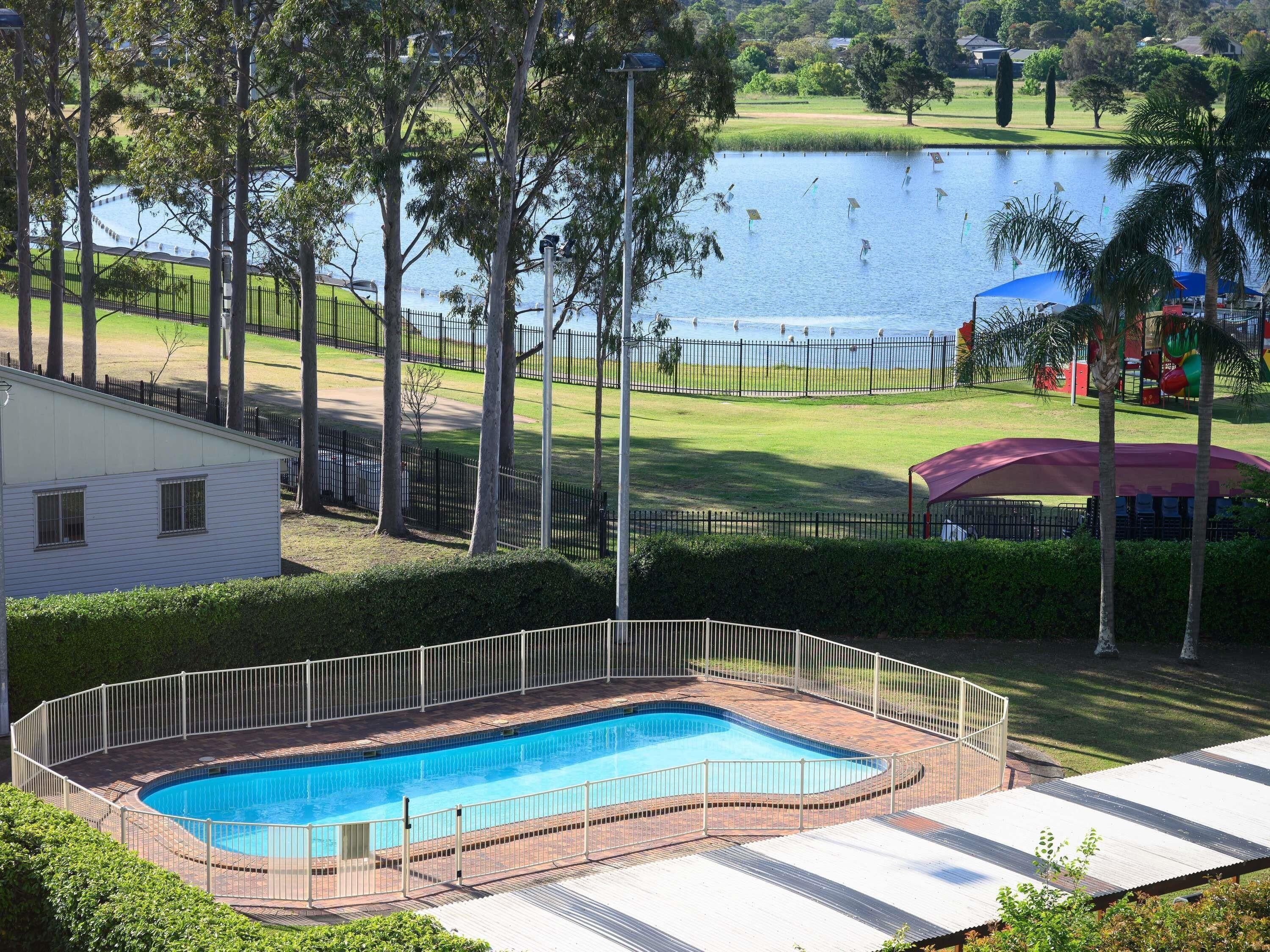 A swimming pool with a surrounding fence, a grassy area, and a body of water in the background.