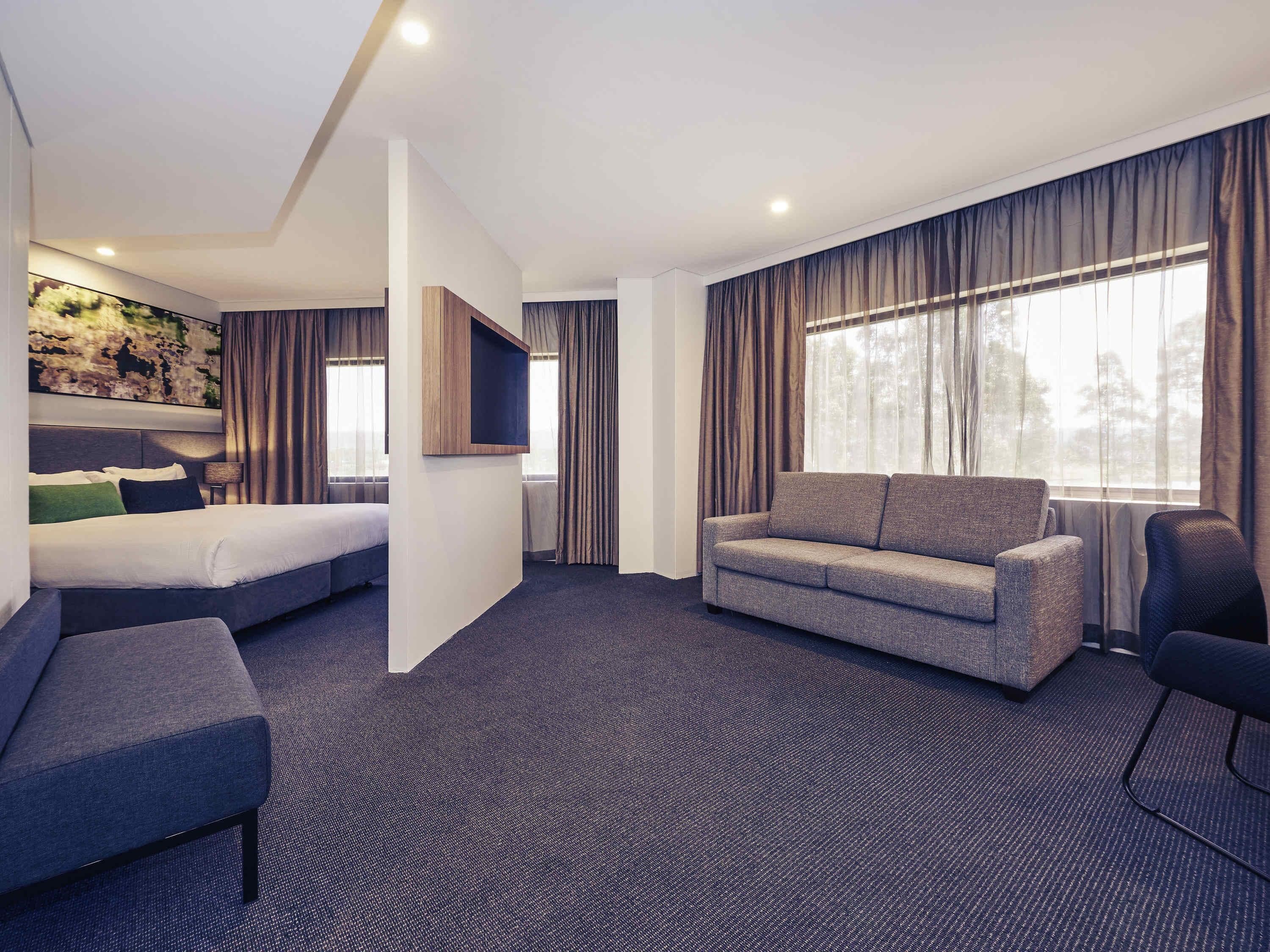 A hotel room with a bed, a sofa, a small table, and a TV.