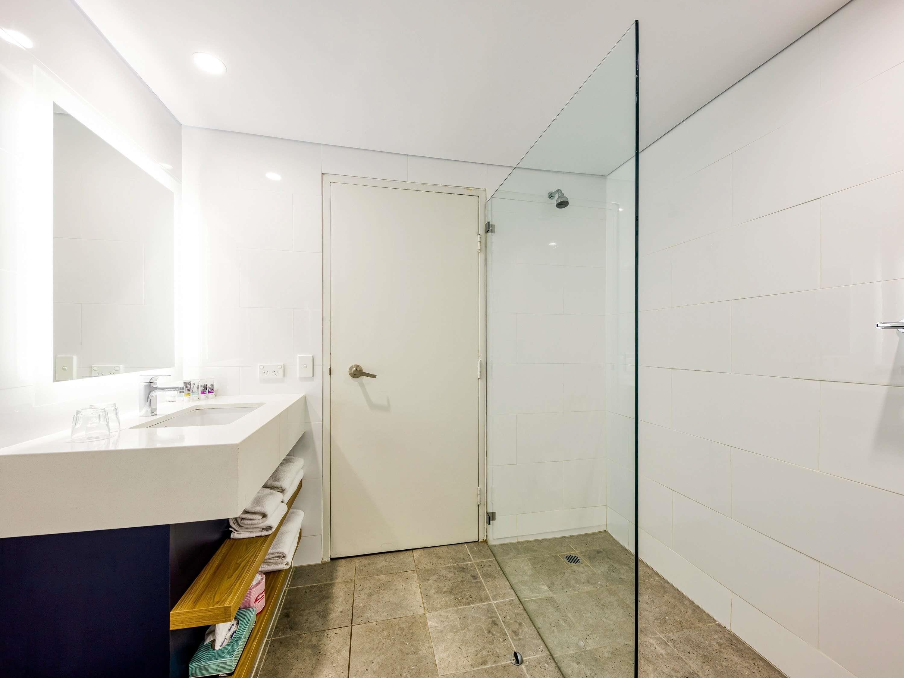Un baño moderno con cabina de ducha de vidrio, tocador blanco con espejo y repisa con toallas.