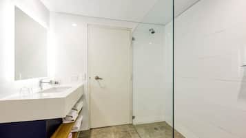 Un baño moderno con cabina de ducha de vidrio, tocador blanco con espejo y repisa con toallas.