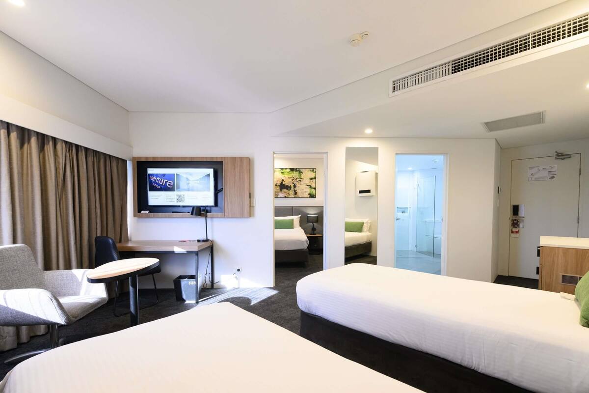 A hotel room with two beds, a desk, a chair, a TV, and a bathroom visible through an open door.