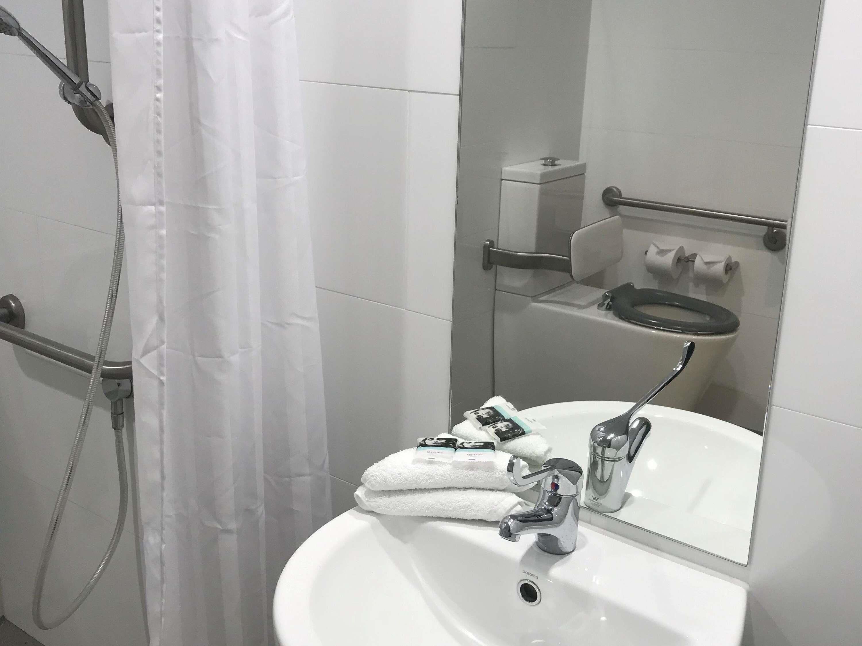Une salle de bain avec un lavabo blanc, un miroir, une douche avec un rideau et des toilettes.
