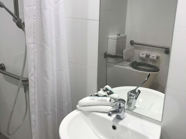 A bathroom with a white sink, a mirror, a shower with a curtain, and a toilet.