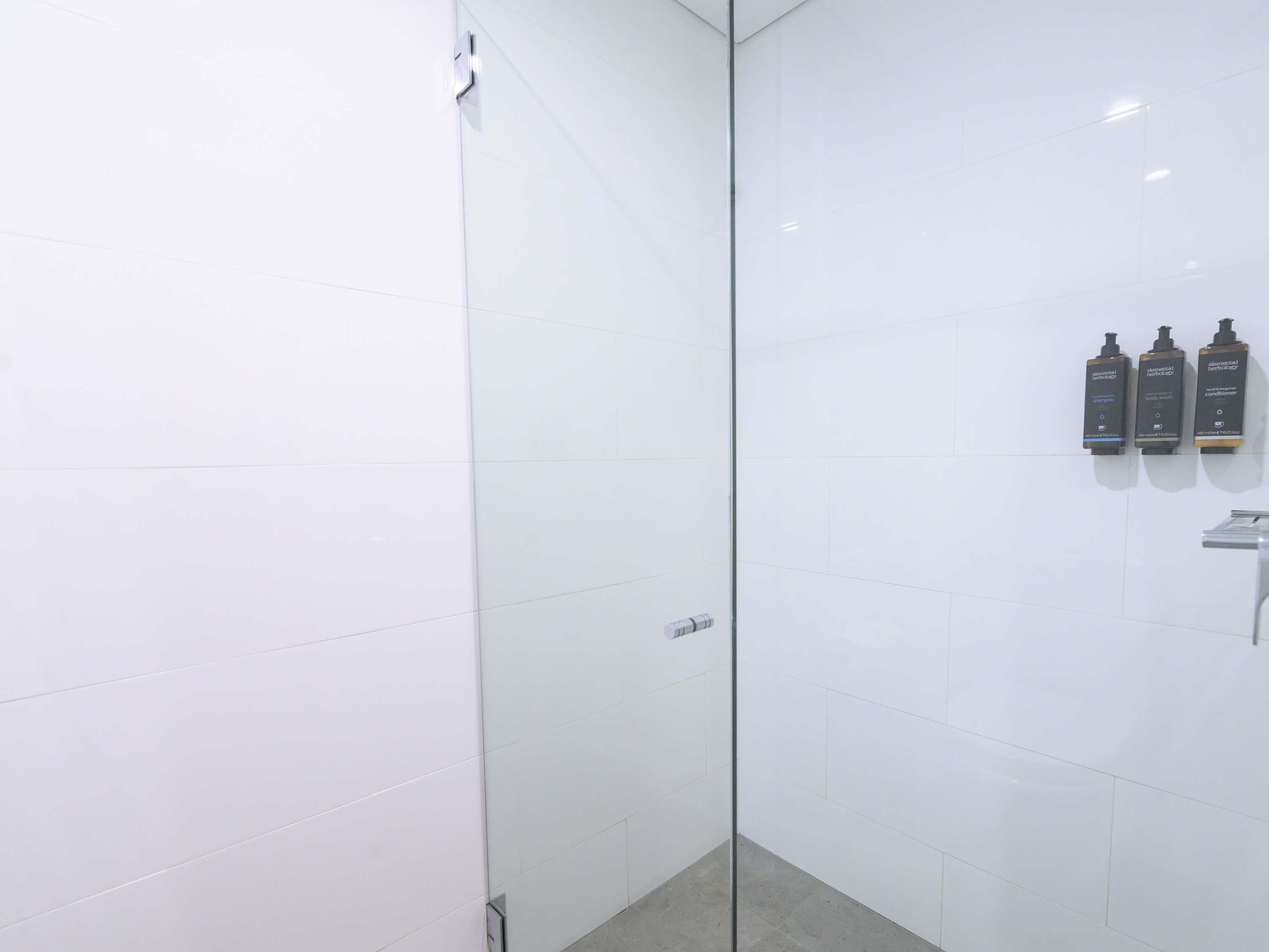 Une salle de bain moderne avec des carreaux blancs, une douche en verre et trois étagères murales pour les articles de toilette.