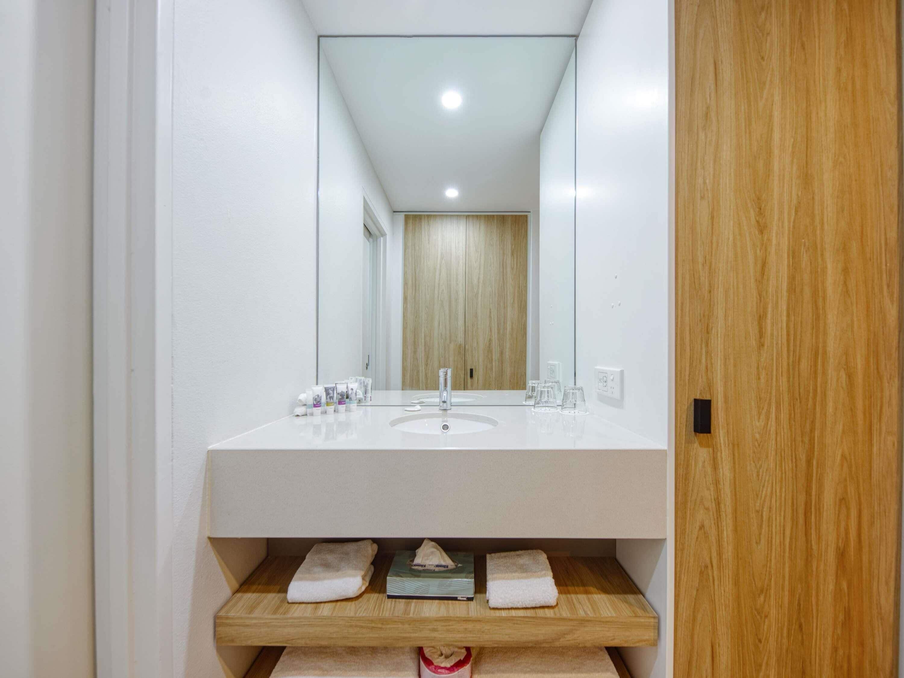 A modern bathroom with a white sink, mirror, and wooden vanity.