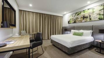 A hotel room with a bed, desk, chair, and a large abstract painting on the wall.