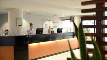 A reception desk with a receptionist, a framed certificate on the wall, and a window with a view of the outside.