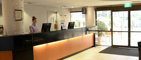 A reception area with a counter, a receptionist, a computer, and a door leading outside.