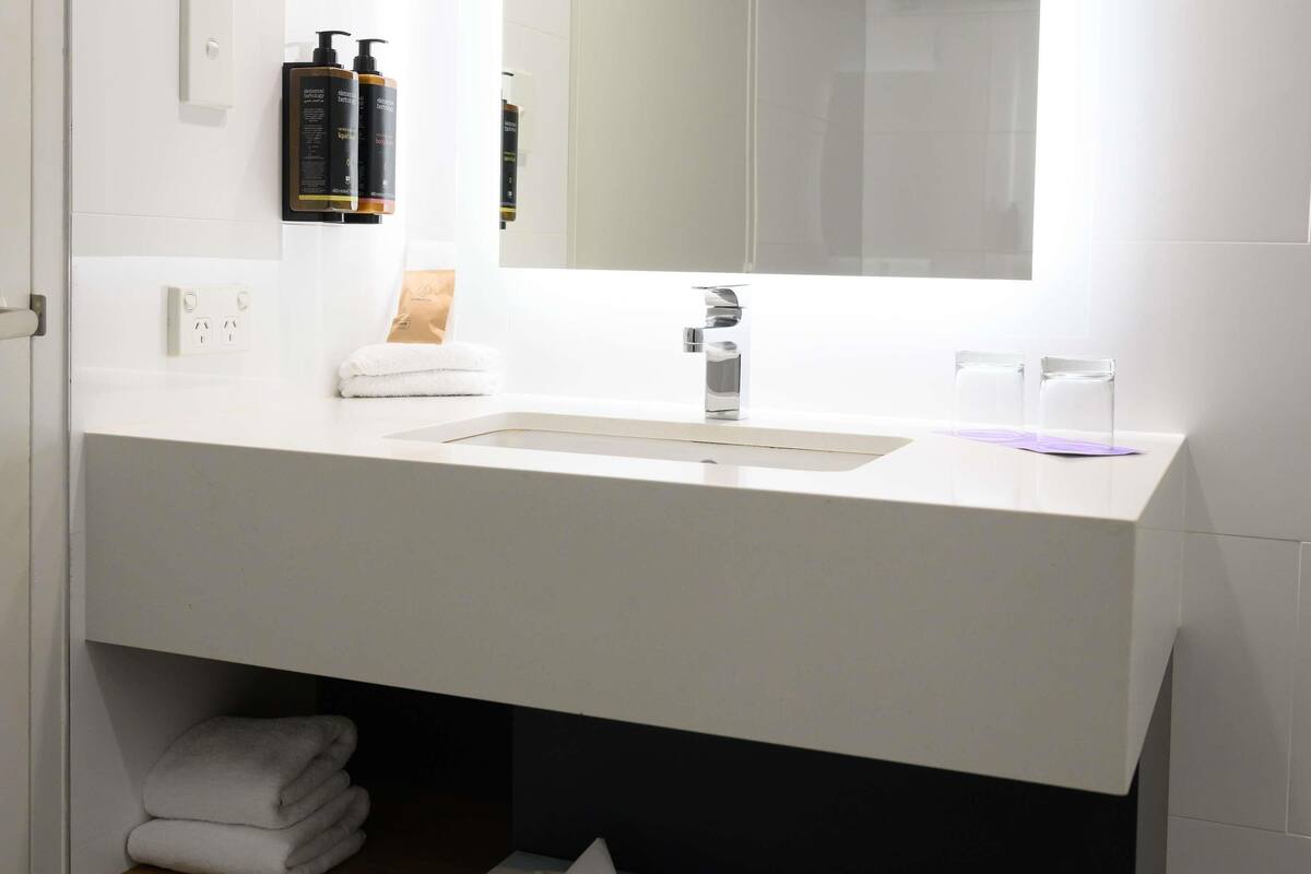 A modern bathroom with a white sink, a mirror, and toiletries on the wall.