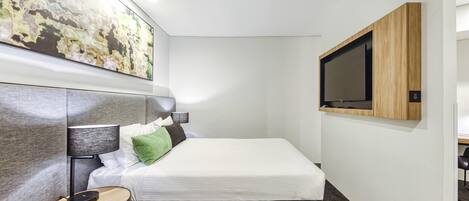 Una habitación de hotel moderna con cama, mesita de noche, lámpara, obra de arte y televisor montado en la pared.