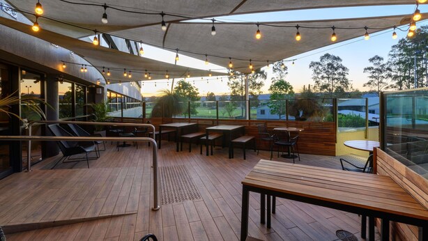 An outdoor patio with wooden tables and chairs, string lights, and a view of the surrounding landscape.