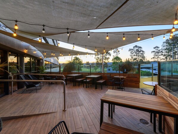 An outdoor patio with wooden tables and chairs, string lights, and a view of the surrounding landscape. - Mercure Penrith (Penrith)