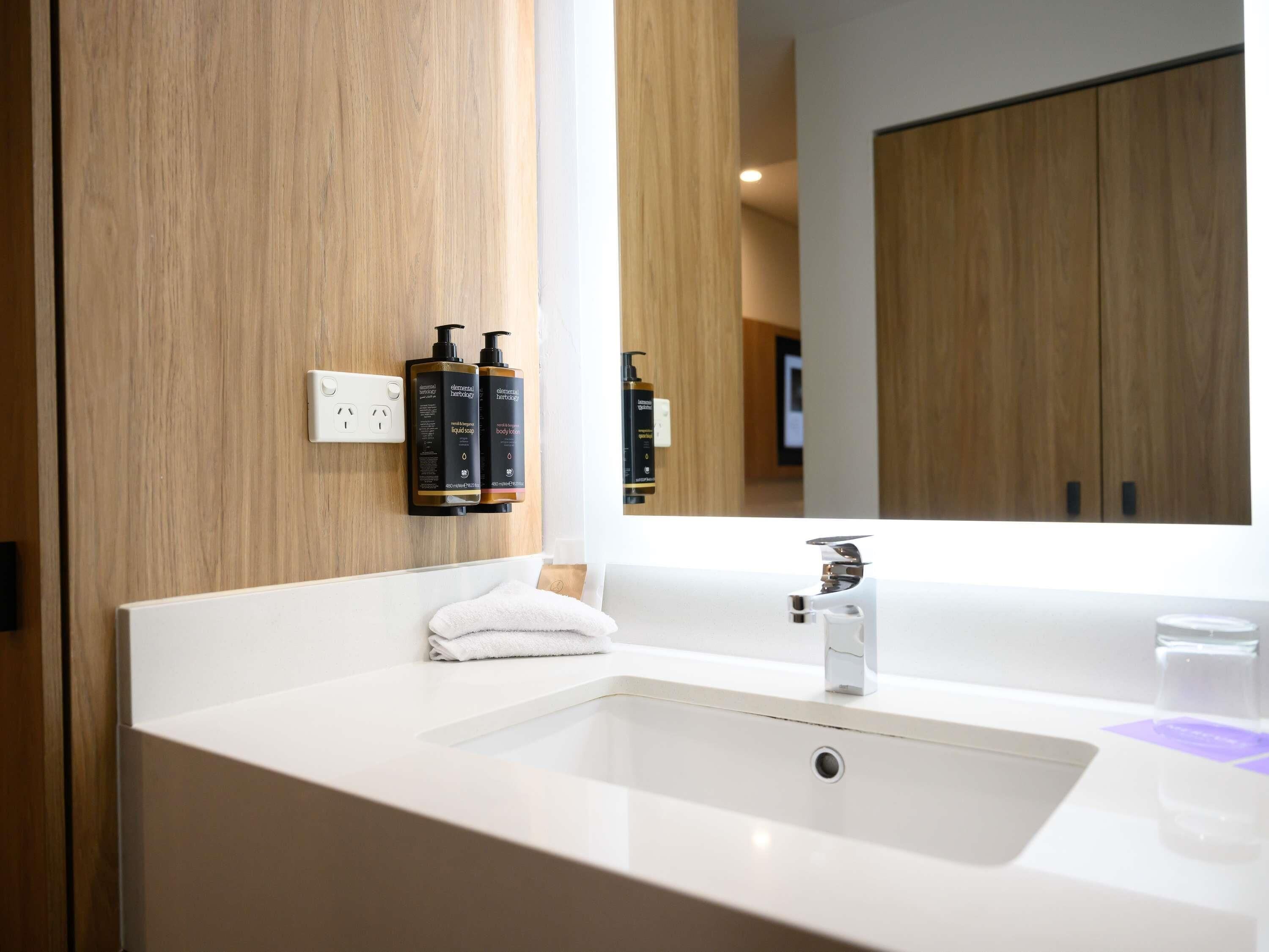 Un baño moderno con un lavabo blanco, un espejo grande, paneles de madera y dos botellas de loción corporal.