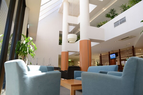 Eine moderne Lobby mit Sitzgelegenheiten, einem Empfangstresen und einem Fernsehbildschirm.