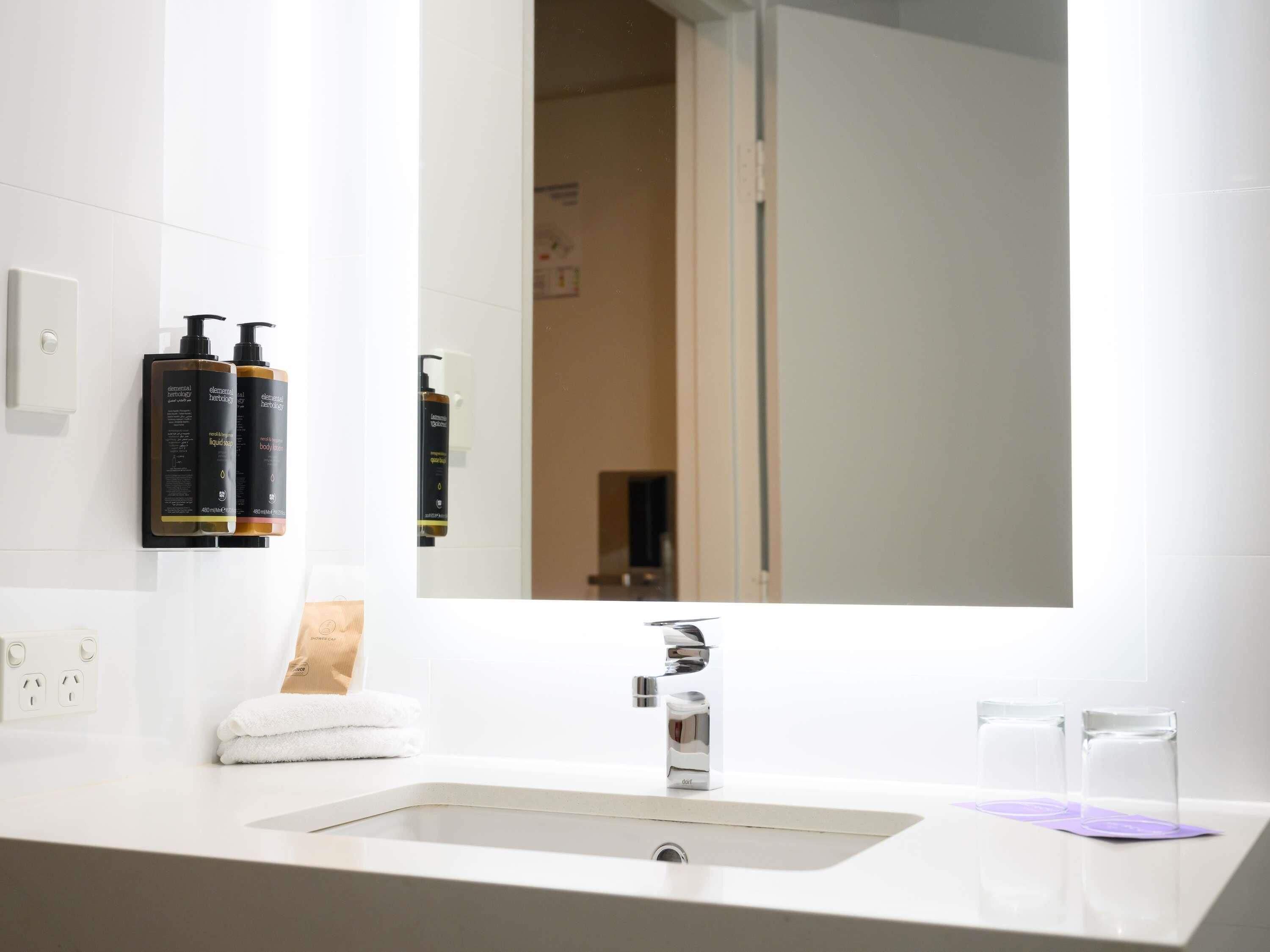 A bathroom with a white sink, a mirror, and two bottles of Elemental Body Lotion.