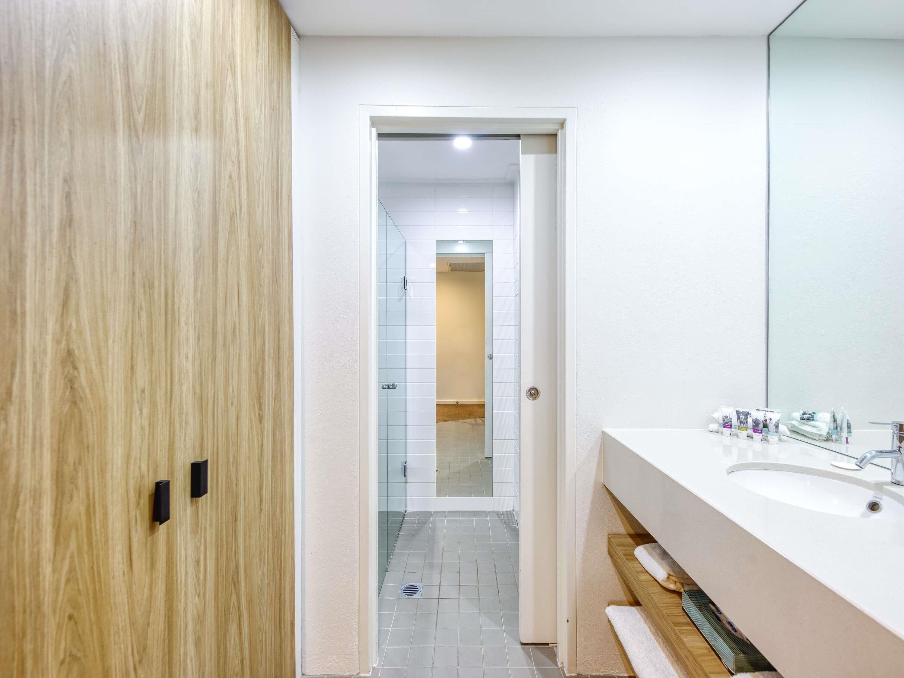 A modern bathroom with a wooden door, a large mirror, and a white sink.