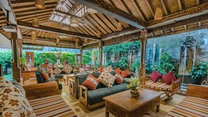 A spacious room with a high ceiling, wooden furniture, and a large window overlooking a lush garden. - Rama Garden Hotel (Legian)