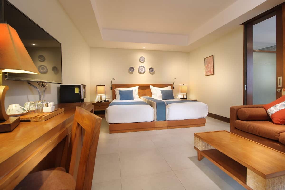 A hotel room with a bed, bedside tables, a desk, a chair, a sofa, and a TV.