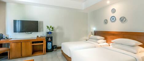 A hotel room with a wooden desk, a flat-screen TV, two beds with white bedding, and a wall-mounted coffee machine.