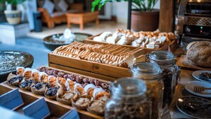 A bakery display with various pastries and bread, a coffee machine, and potted plants in the background. - Rama Garden Hotel (Legian)