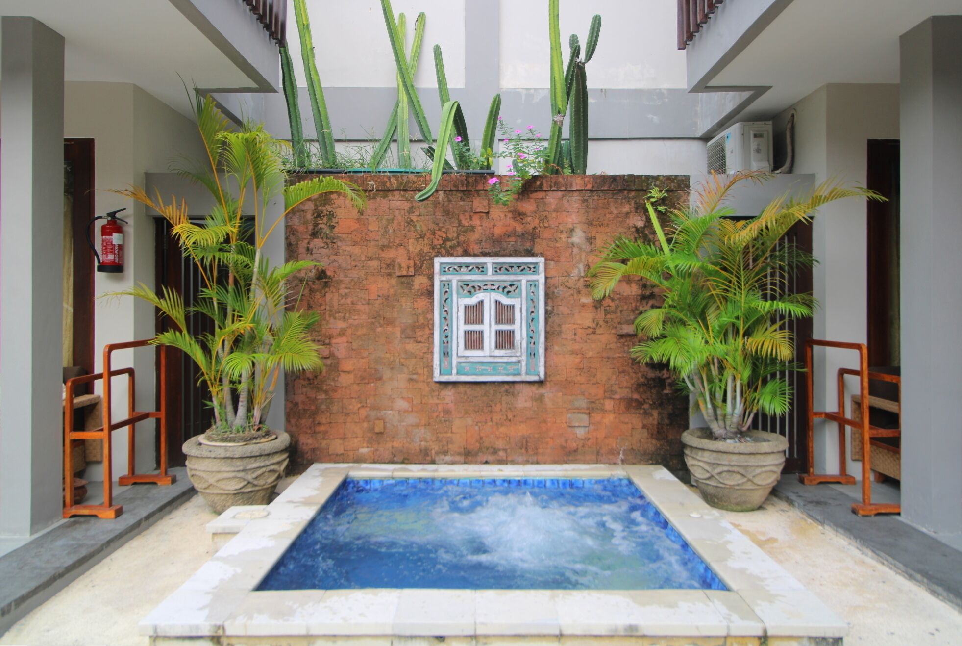 Zona de piscina con pared de ladrillo, plantas en macetas y ventana con marco decorativo.
