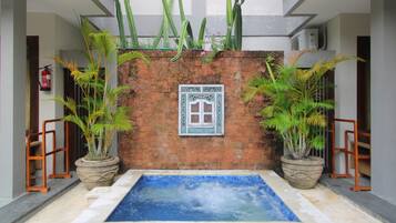 Zona de piscina con pared de ladrillo, plantas en macetas y ventana con marco decorativo.
