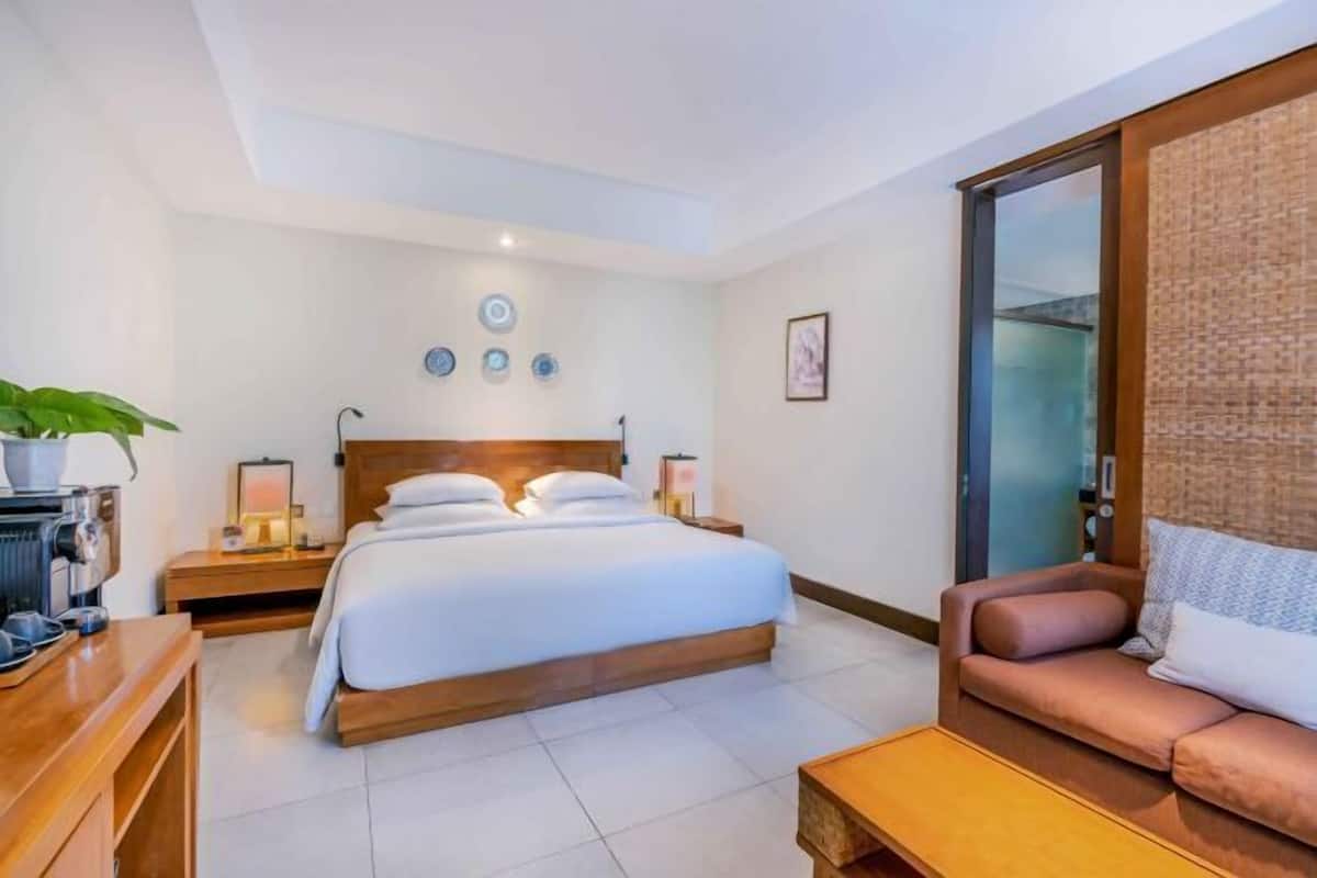 A hotel room with a bed, a sofa, a coffee machine, a nightstand, and a wall with decorative plates.