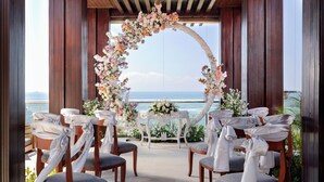 Decoración para una boda al aire libre con sillas de madera y un arco floral, con vistas a un cuerpo de agua.