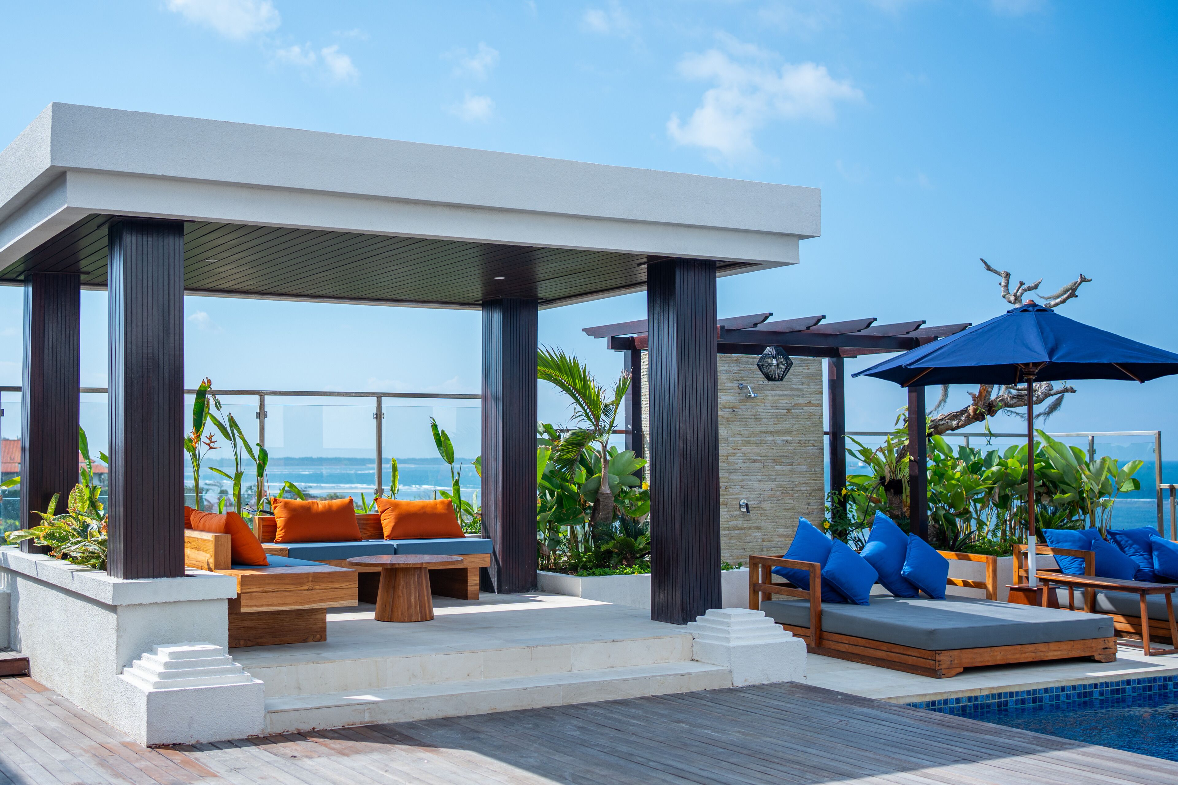 A rooftop pool area with a covered seating area, lounge chairs, and a view of the ocean.