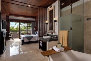 Habitación de hotel con cama, escritorio, baño con ducha de vidrio y vistas a árboles.
