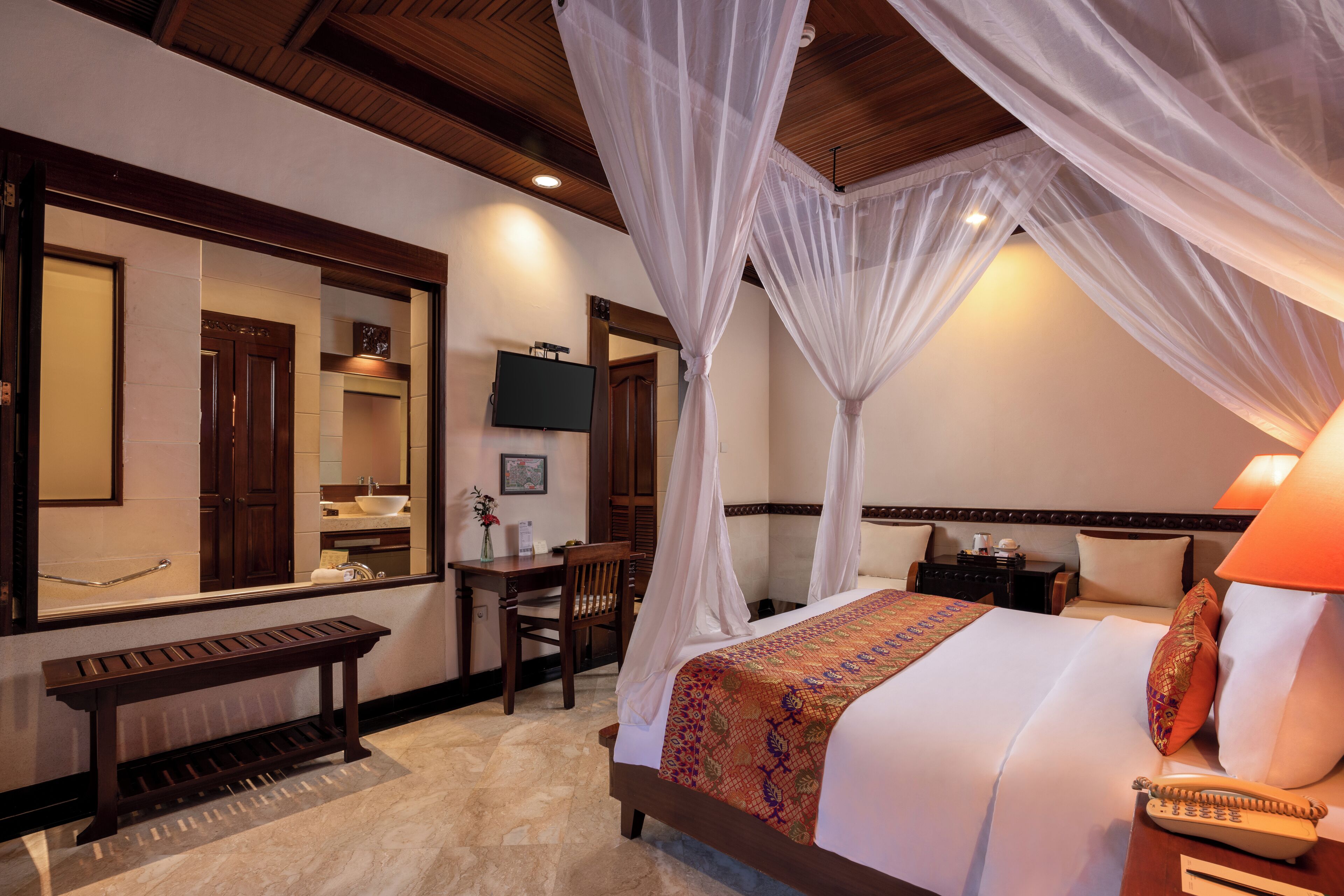 A hotel room with a bed, bedside table, chair, desk, and a television.