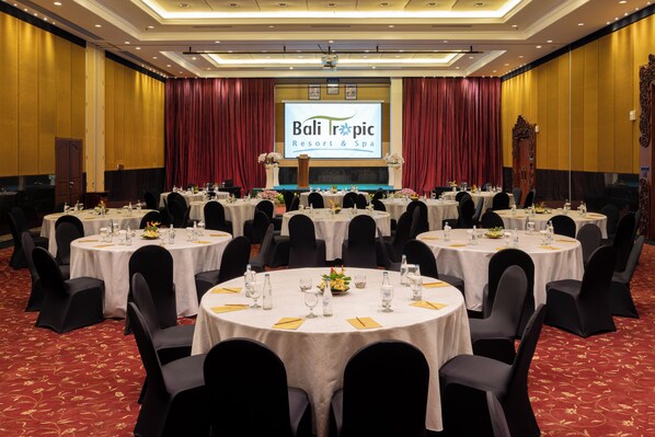 A conference room at Bali Tropic Resort & Spa with multiple round tables, black chairs, and a stage with a presentation screen. - Bali Tropic Resort & Spa (Nusa Dua)