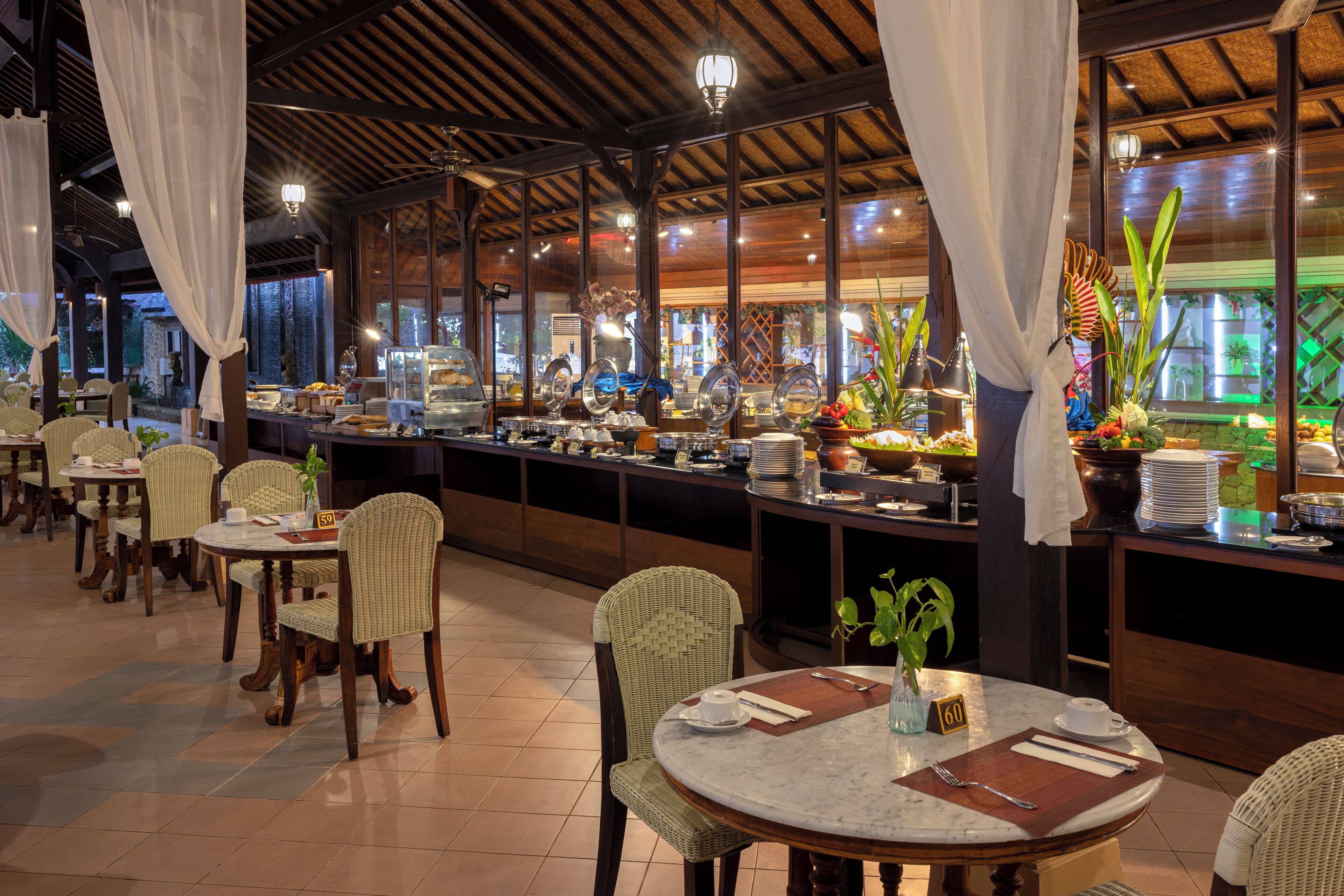 Un restaurante con mesas redondas, sillas de mimbre y una zona de bufé con diferentes opciones de comida.