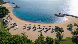 A beach with sun loungers and umbrellas, a small island with a gazebo, and clear blue waters. - Bali Tropic Resort & Spa (Nusa Dua)