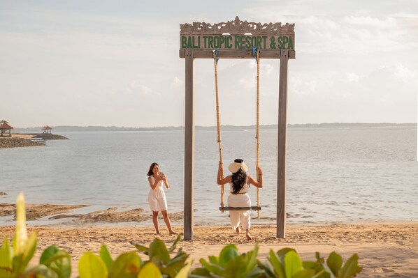 Un columpio de madera con un cartel que dice "Bali Tropic Resort & Spa" junto a la playa.