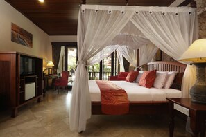 A bedroom with a four-poster bed, a desk with a chair, and a television. - Bali Tropic Resort & Spa (Nusa Dua)