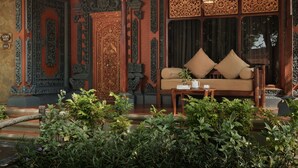 A traditional room with ornate wooden carvings, a sofa with cushions, and a small table with a cup and book. - Bali Tropic Resort & Spa (Nusa Dua)