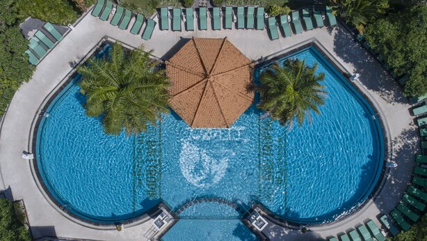 An aerial view of a circular swimming pool with multiple lounge areas and palm trees. - Bali Tropic Resort & Spa (Nusa Dua)