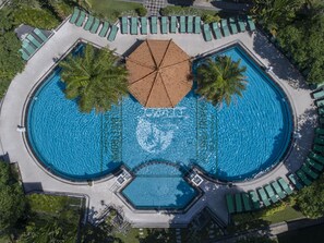Vista aérea de una piscina circular con varias zonas de descanso y palmeras.