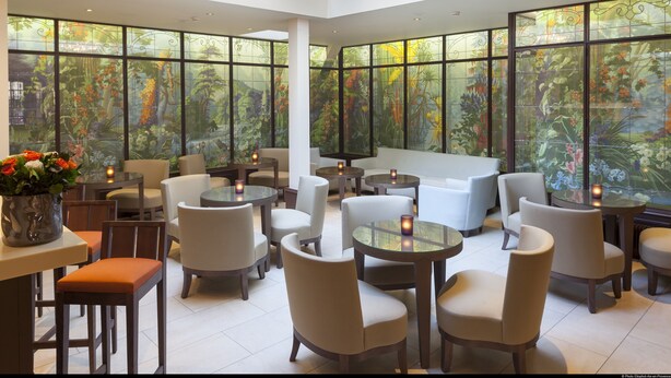 A spacious indoor area with multiple seating arrangements, large windows with floral designs, and a central chandelier. - Hotel De L'Universite (Paris)