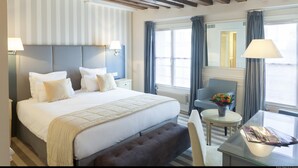 A hotel room with a large bed, a small table with a vase of flowers, a chair, and a window with curtains. - Hotel De L'Universite (Paris)