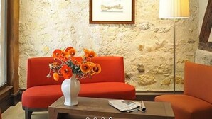 A room with a stone wall, a framed picture, a white vase with flowers, and an orange sofa. - Hotel De L'Universite (Paris)