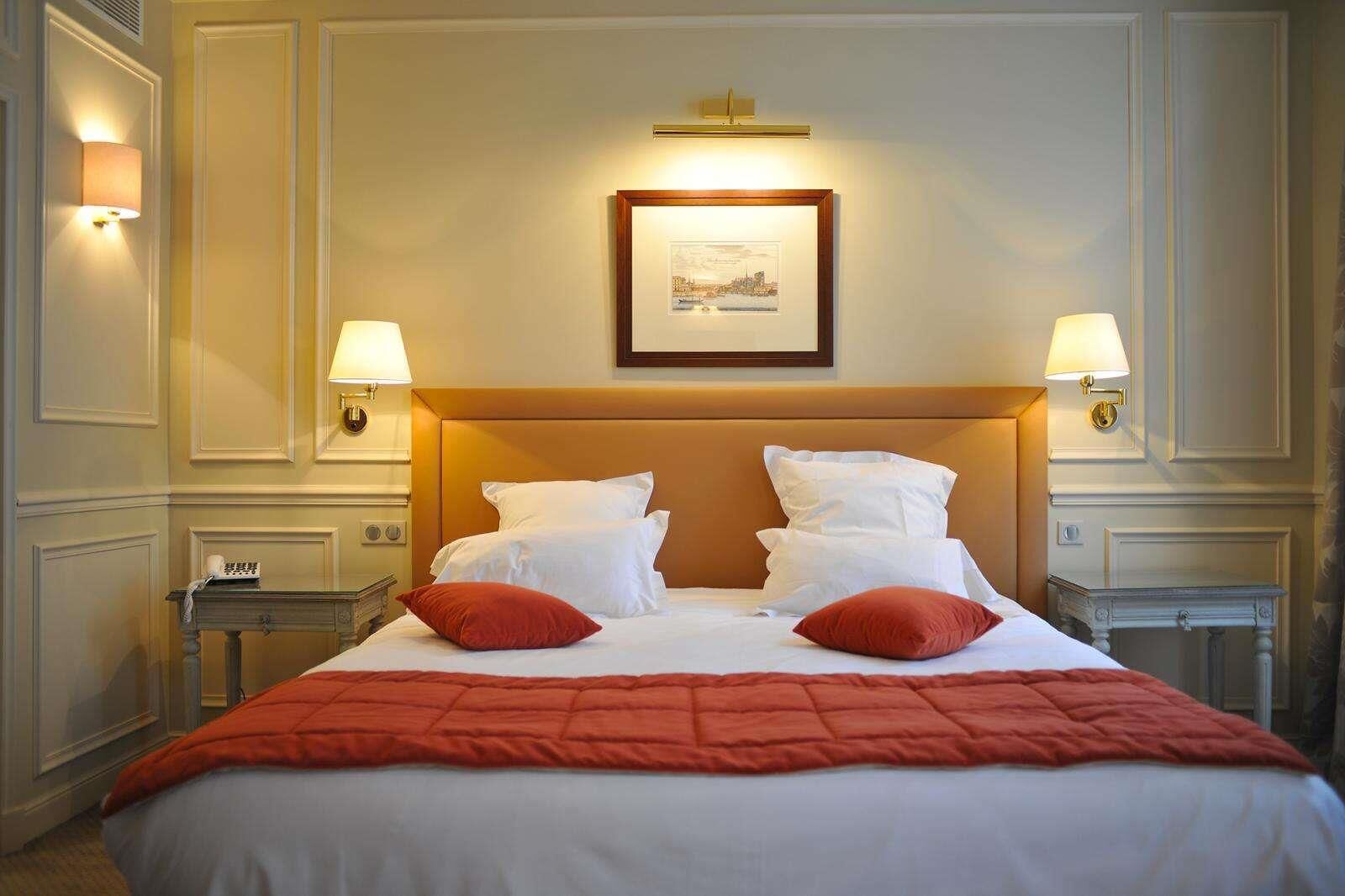 A hotel room with a large bed, two bedside tables, a framed picture on the wall, and wall-mounted lamps.