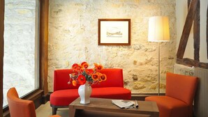 A room with a stone wall, a red sofa, a white vase with flowers, a framed picture, and a floor lamp. - Hotel De L'Universite (Paris)