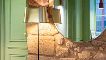 Una habitación con una puerta verde, pared de piedra, espejo redondo y sillones anaranjados.