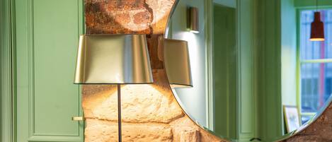 A room with a green door, a stone wall, a round mirror, and orange armchairs.