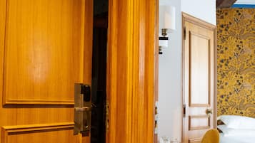 Habitación de hotel con puerta de madera, cama, mesita de noche, silla y alfombra estampada.
